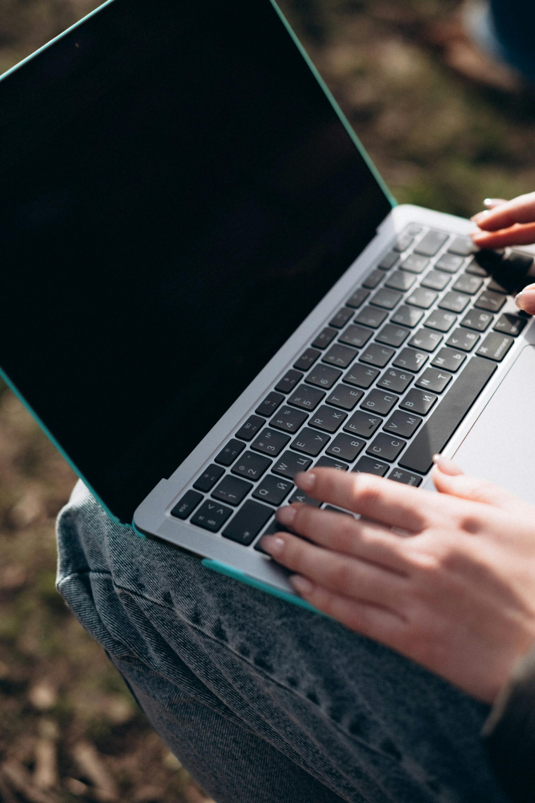 Person typing on a laptop while seated outdoors, showcasing portable technology use.